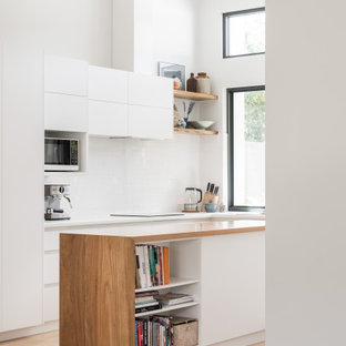 Contemporary l-shaped kitchen in Other with flat-panel cabinets, white cabinets, wood benchtops, white splashback, light hardwood floors, with island, beige floor, brown benchtop and vaulted.