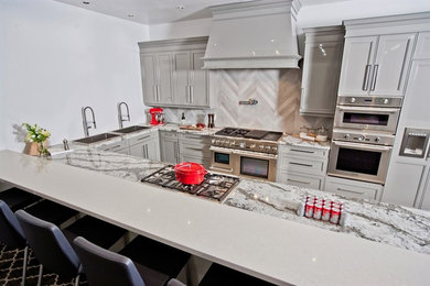 Large trendy galley concrete floor eat-in kitchen photo in Toronto with a drop-in sink, recessed-panel cabinets, gray cabinets, granite countertops, gray backsplash, stone tile backsplash, stainless steel appliances and a peninsula
