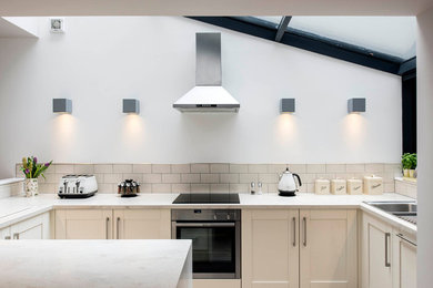 Traditional u-shaped kitchen in Other with a built-in sink, shaker cabinets, beige cabinets, beige splashback, metro tiled splashback and stainless steel appliances.