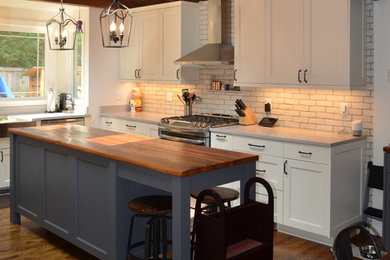 Eat-in kitchen - mid-sized farmhouse u-shaped medium tone wood floor and brown floor eat-in kitchen idea in Seattle with a farmhouse sink, shaker cabinets, white cabinets, quartz countertops, white backsplash, brick backsplash, stainless steel appliances and an island