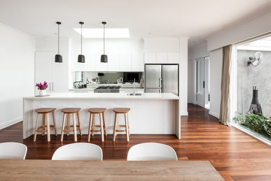 Idéer för mellanstora funkis linjära vitt kök och matrum, med luckor med upphöjd panel, vita skåp, bänkskiva i kvarts, spegel som stänkskydd, en köksö, en undermonterad diskho, stänkskydd med metallisk yta, rostfria vitvaror, mörkt trägolv och brunt golv