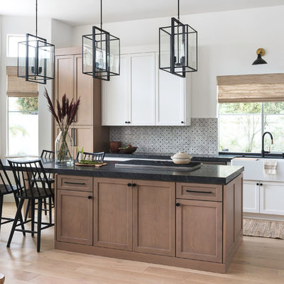Mid-sized transitional l-shaped light wood floor eat-in kitchen photo in San Diego with a farmhouse sink, shaker cabinets, light wood cabinets, granite countertops, beige backsplash, terra-cotta backsplash, stainless steel appliances, an island and black countertops