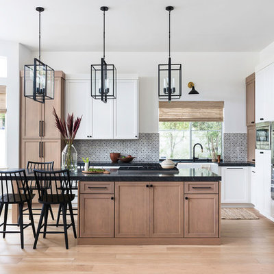 Inspiration for a mid-sized transitional l-shaped brown floor and medium tone wood floor kitchen remodel in San Diego with a farmhouse sink, shaker cabinets, granite countertops, terra-cotta backsplash, stainless steel appliances, an island, black countertops, medium tone wood cabinets and gray backsplash