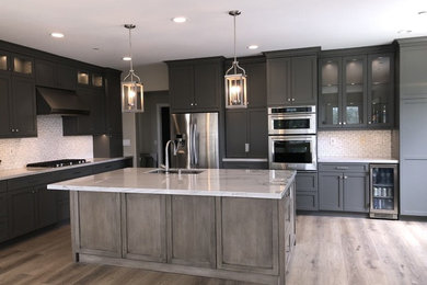 Example of a large trendy l-shaped eat-in kitchen design in Orange County with a single-bowl sink, recessed-panel cabinets, gray cabinets, quartzite countertops, white backsplash, stone tile backsplash, stainless steel appliances, an island and white countertops