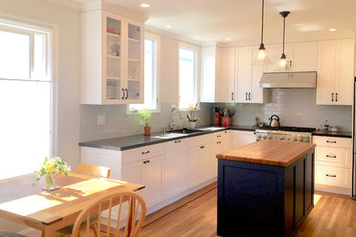 Cette image montre une cuisine américaine bohème avec un placard à porte shaker, des portes de placard blanches, un plan de travail en quartz modifié, une crédence grise, une crédence en céramique, parquet clair et îlot.