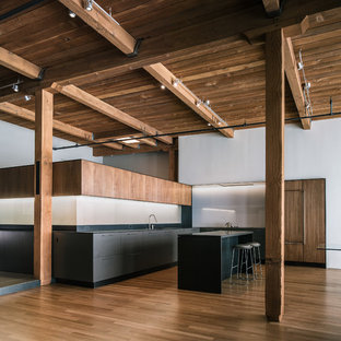 Zweizeilige Industrial Wohnküche mit flächenbündigen Schrankfronten, hellbraunen Holzschränken, Küchenrückwand in Schwarz und Elektrogeräten mit Frontblende in San Francisco