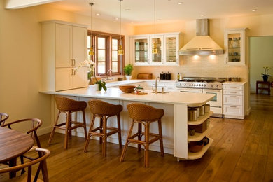 Example of a classic medium tone wood floor kitchen design in San Francisco with an undermount sink, glass-front cabinets, white cabinets, quartzite countertops, white backsplash, ceramic backsplash, stainless steel appliances and a peninsula