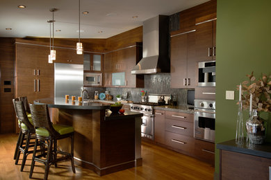 Inredning av ett modernt stort kök, med en nedsänkt diskho, släta luckor, skåp i mörkt trä, bänkskiva i koppar, grönt stänkskydd, stänkskydd i sten, rostfria vitvaror, ljust trägolv och en köksö