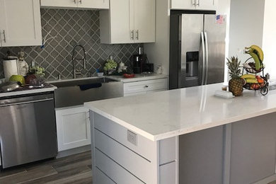 Mid-sized beach style l-shaped ceramic tile and brown floor kitchen pantry photo in Orange County with a farmhouse sink, shaker cabinets, white cabinets, quartzite countertops, gray backsplash, ceramic backsplash, stainless steel appliances and an island
