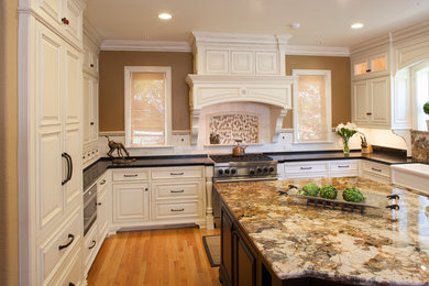 Example of a classic u-shaped medium tone wood floor eat-in kitchen design in San Francisco with a farmhouse sink, beaded inset cabinets, white cabinets, granite countertops, white backsplash, stone tile backsplash, paneled appliances and an island