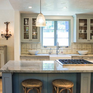 Immagine di una cucina chic con lavello stile country, ante di vetro, ante grigie, paraspruzzi beige e elettrodomestici da incasso