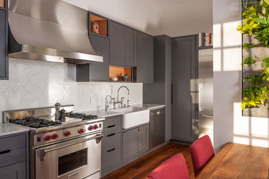 Bild på ett mellanstort lantligt linjärt kök och matrum, med en rustik diskho, släta luckor, grå skåp, bänkskiva i kvartsit, vitt stänkskydd, stänkskydd i mosaik, rostfria vitvaror och mellanmörkt trägolv