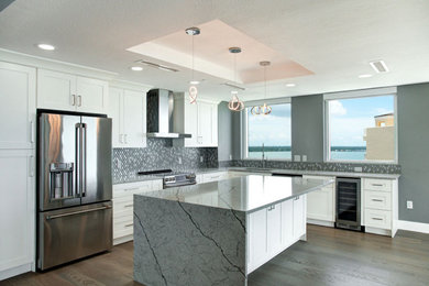 Inspiration for a mid-sized contemporary u-shaped medium tone wood floor, brown floor and tray ceiling open concept kitchen remodel in Tampa with an undermount sink, recessed-panel cabinets, white cabinets, granite countertops, multicolored backsplash, mosaic tile backsplash, stainless steel appliances, an island and gray countertops