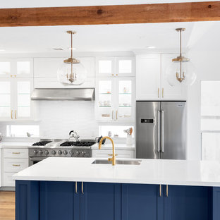 This is an example of a mid-sized transitional l-shaped eat-in kitchen in Houston with an undermount sink, recessed-panel cabinets, blue cabinets, quartz benchtops, white splashback, subway tile splashback, stainless steel appliances, light hardwood floors, with island, orange floor and white benchtop.