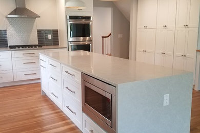 Example of a large u-shaped medium tone wood floor and multicolored floor open concept kitchen design in New York with an undermount sink, recessed-panel cabinets, white cabinets, solid surface countertops, black backsplash, ceramic backsplash, stainless steel appliances and an island