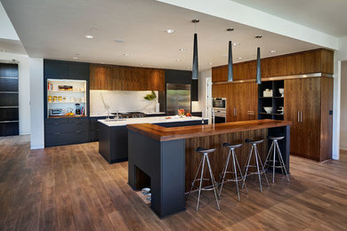 Kitchen - large contemporary dark wood floor kitchen idea in Portland with an undermount sink, flat-panel cabinets, dark wood cabinets, white backsplash, stainless steel appliances and two islands