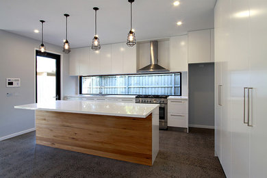 Medium sized modern single-wall open plan kitchen in Melbourne with a double-bowl sink, flat-panel cabinets, white cabinets, composite countertops, window splashback, stainless steel appliances, concrete flooring and an island.