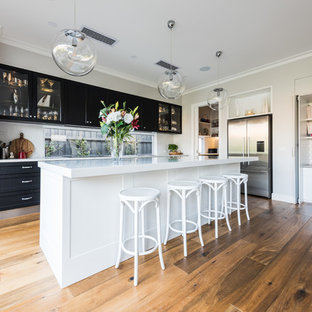 Inspiration for a transitional kitchen in Melbourne with shaker cabinets, black cabinets, window splashback, stainless steel appliances, medium hardwood floors, with island, brown floor and white benchtop.