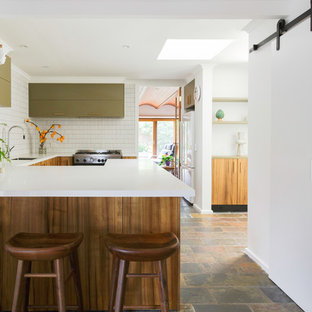 This is an example of a large contemporary u-shaped kitchen in Melbourne with green cabinets, solid surface benchtops, white splashback, stainless steel appliances, limestone floors, white benchtop, an undermount sink, flat-panel cabinets, matchstick tile splashback and a peninsula.