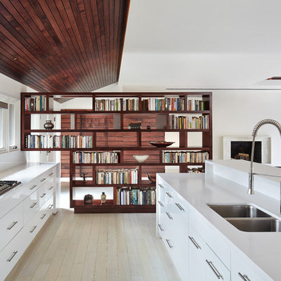 Example of a danish galley light wood floor open concept kitchen design in New York with a double-bowl sink, flat-panel cabinets, white cabinets, white backsplash, glass sheet backsplash and an island