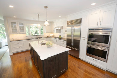 Eat-in kitchen - large transitional l-shaped dark wood floor and brown floor eat-in kitchen idea in New York with a double-bowl sink, shaker cabinets, white cabinets, quartz countertops, white backsplash, ceramic backsplash, stainless steel appliances and an island