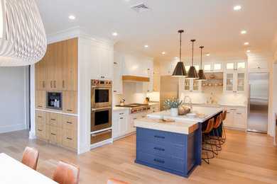 Large transitional u-shaped light wood floor and yellow floor eat-in kitchen photo in New York with a farmhouse sink, flat-panel cabinets, white cabinets, quartzite countertops, white backsplash, stone slab backsplash, stainless steel appliances, two islands and white countertops