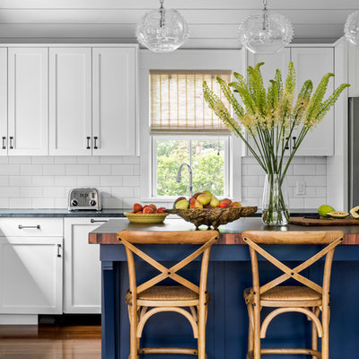 Enclosed kitchen - small coastal l-shaped medium tone wood floor enclosed kitchen idea in Boston with a farmhouse sink, recessed-panel cabinets, white cabinets, soapstone countertops, white backsplash, subway tile backsplash, stainless steel appliances, an island and black countertops