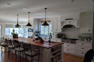 Inspiration for a large transitional l-shaped medium tone wood floor and brown floor open concept kitchen remodel in Boston with a farmhouse sink, shaker cabinets, white cabinets, stainless steel appliances and an island