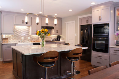 Example of a mid-sized transitional l-shaped medium tone wood floor eat-in kitchen design in Atlanta with shaker cabinets, gray cabinets, black appliances, an island, a farmhouse sink, granite countertops, brown backsplash and ceramic backsplash