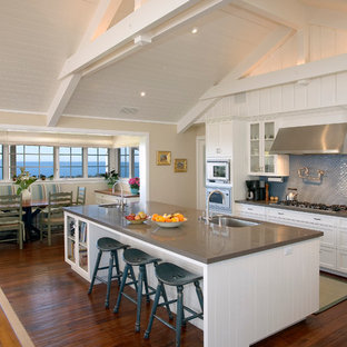 This is an example of a large traditional galley open plan kitchen in Santa Barbara with a single-bowl sink, quartz benchtops, blue splashback, glass-front cabinets, white cabinets, glass tile splashback, stainless steel appliances, with island and dark hardwood floors.