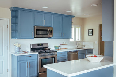 Immagine di una cucina bohémian di medie dimensioni con lavello da incasso, ante in stile shaker, ante blu, top in quarzo composito, paraspruzzi bianco, paraspruzzi in gres porcellanato, elettrodomestici in acciaio inossidabile, pavimento in vinile e penisola