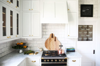 Example of an arts and crafts kitchen design in Albuquerque with a farmhouse sink, recessed-panel cabinets, white cabinets, marble countertops, white backsplash, ceramic backsplash and black appliances