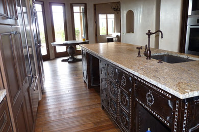 Example of a large tuscan u-shaped medium tone wood floor open concept kitchen design in Albuquerque with an island, distressed cabinets, a drop-in sink and stainless steel appliances
