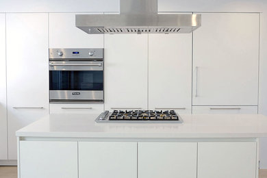 Minimalist kitchen photo in Los Angeles with white cabinets, stainless steel appliances and an island
