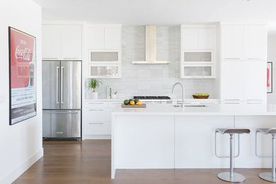 Mid-sized minimalist galley medium tone wood floor open concept kitchen photo in Los Angeles with an undermount sink, flat-panel cabinets, white cabinets, quartz countertops, white backsplash, stone tile backsplash, stainless steel appliances and an island