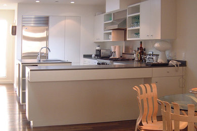 Example of a small minimalist u-shaped medium tone wood floor and brown floor open concept kitchen design in Los Angeles with an undermount sink, flat-panel cabinets, white cabinets, solid surface countertops, stainless steel appliances and an island