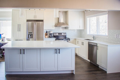 Inspiration for a mid-sized transitional l-shaped laminate floor eat-in kitchen remodel in Calgary with an undermount sink, shaker cabinets, white cabinets, quartz countertops, white backsplash, glass tile backsplash, stainless steel appliances and an island