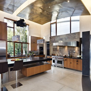 Réalisation d'une grand cuisine ouverte design en L avec un placard à porte plane, des portes de placard en bois brun, un plan de travail en stéatite, une crédence marron, un électroménager en acier inoxydable, une crédence en ardoise, un évier encastré, béton au sol, un îlot central et un sol gris.