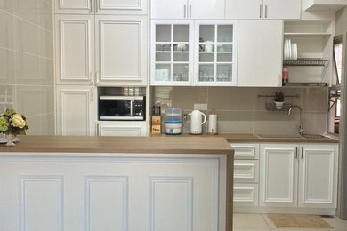 Example of a mid-sized classic single-wall ceramic tile eat-in kitchen design in Other with a double-bowl sink, beaded inset cabinets, white cabinets, wood countertops, beige backsplash, mosaic tile backsplash, black appliances and an island