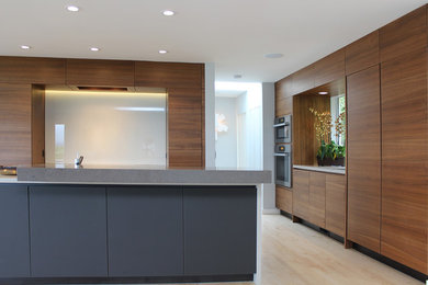 Example of a minimalist light wood floor open concept kitchen design in San Francisco with flat-panel cabinets, dark wood cabinets, quartz countertops, white backsplash, stone slab backsplash, paneled appliances and an island