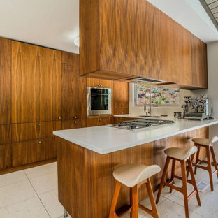Mittelgroße Retro Küche mit Doppelwaschbecken, flächenbündigen Schrankfronten, Mineralwerkstoff-Arbeitsplatte, Küchengeräten aus Edelstahl, Terrazzo-Boden, Halbinsel, weißem Boden, weißer Arbeitsplatte, freigelegten Dachbalken und hellbraunen Holzschränken in Los Angeles