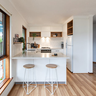 This is an example of a scandinavian u-shaped kitchen in Adelaide with an undermount sink, flat-panel cabinets, white cabinets, white splashback, subway tile splashback, white appliances, brown floor, white benchtop, quartz benchtops and laminate floors.