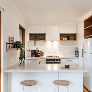 Contemporary u-shaped kitchen in Adelaide with an undermount sink, flat-panel cabinets, white cabinets, white splashback, white appliances, a peninsula, brown floor, white benchtop and laminate floors.