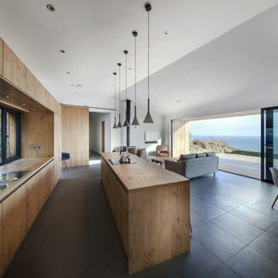 This is an example of a large contemporary galley open plan kitchen in Hampshire with flat-panel cabinets, medium wood cabinets, composite countertops, metallic splashback, glass sheet splashback, stainless steel appliances, ceramic flooring, an island and grey floors.