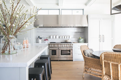 Example of a transitional l-shaped medium tone wood floor and brown floor eat-in kitchen design in Los Angeles with shaker cabinets, white cabinets, gray backsplash, stainless steel appliances, an island and white countertops