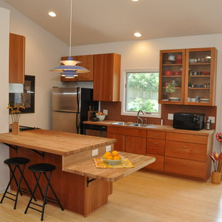 Inspiration for a small country galley open plan kitchen in Omaha with a double-bowl sink, flat-panel cabinets, medium wood cabinets, wood benchtops, orange splashback, terra-cotta splashback, stainless steel appliances, bamboo floors and a peninsula.