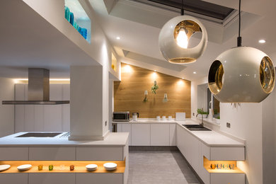 Photo of a medium sized modern l-shaped kitchen/diner in Cheshire with a double-bowl sink, flat-panel cabinets, white cabinets, quartz worktops, white splashback, stainless steel appliances and an island.