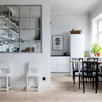 Eat-in kitchen - small scandinavian u-shaped light wood floor and beige floor eat-in kitchen idea in New York with flat-panel cabinets, white cabinets, white appliances, no island and black countertops