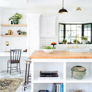 Idées déco pour une cuisine ouverte scandinave en U de taille moyenne avec un évier de ferme, un placard avec porte à panneau encastré, des portes de placard blanches, une crédence blanche, une crédence en carrelage métro, un électroménager en acier inoxydable, un sol en carrelage de porcelaine, une péninsule et un plan de travail en bois.
