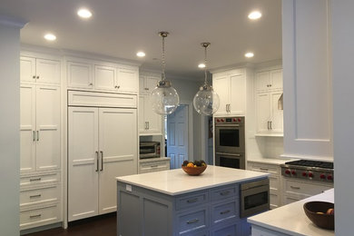 Example of a mid-sized transitional u-shaped dark wood floor and brown floor eat-in kitchen design in New York with a double-bowl sink, raised-panel cabinets, white cabinets, solid surface countertops, white backsplash, subway tile backsplash, stainless steel appliances and an island